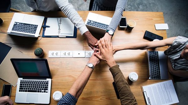 Technology team work with hands in middle of desk with laptops